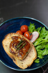 Seared French foie gras and roasted tomatoes on crunchy toast, garnished with fresh greens, are elegantly presented on a unique blue stone plate for a gourmet starter