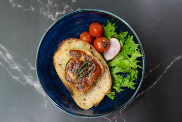 Seared French foie gras and roasted tomatoes on crunchy toast, garnished with fresh greens, are elegantly presented on a unique blue stone plate for a gourmet starter