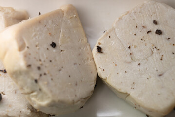 Raw French foie gras block seasoned with whole black peppercorns, ready for gourmet preparation and cooking, emphasizing a culinary process