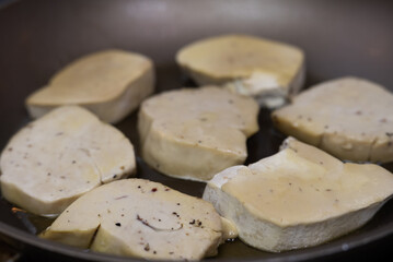 Seared foie gras sizzling in a hot frying pan with rendered fat, creating a golden-brown crust for a classic French gourmet cooking process