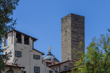 Fototapeta premium Torre del Gombito rising above medieval rooftops in Bergamo Italy, with the dome of Santa Maria Maggiore crowned by a golden Archangel Michael under clear blue sky
