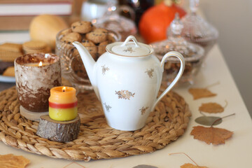 Lit candles, cookies, chocolate, nuts, tea, wine, pumpkins, books, reading glasses and autumn leaves on the table. Autumnal hygge at home. Selective focus.