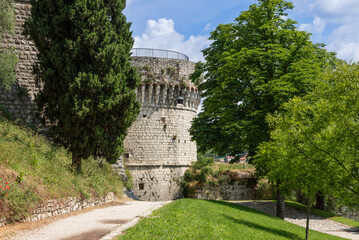 Tower of the French in Brescia Castle rises behind green foliage on warm summer day, a historic...