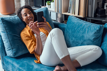 Smiling woman relaxing on sofa using smartphone at home