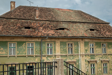 An old historic building with peeling facade, wooden windows, and old roof tiles. Romania, Sibiu.