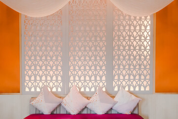 Luxury spa style interior with orange walls, carved wood panel, and pastel cushions on bench. Perfect for wellness branding, hotel decor, tropical lifestyle, or boutique relaxation concepts.
