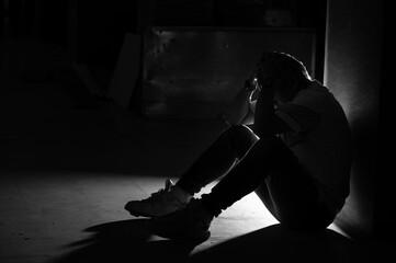 Silhouette man sitting floor shadow darkness loneliness stress anxiety depression despair solitude indoor corner moody dramatic low light black white monochrome profile crouch head hands sneaker
