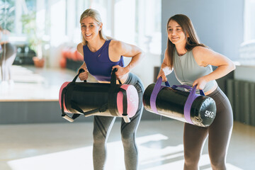 Two sporty women in gym lifting dumbbells wearing sportswear training for strength energy fitness and an active healthy lifestyle