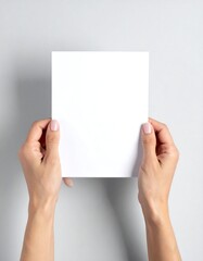 Obraz premium Hands holding a blank square white card against a light gray background