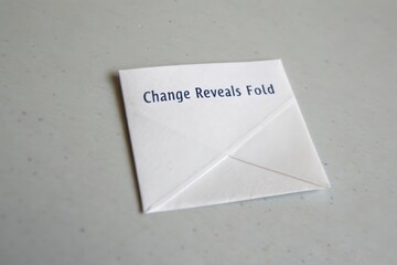 White paper folded into a square shape with a Change Reveals Fold message
