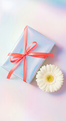 Elegant gift box in iridescent wrapping paper with a red ribbon and a white gerbera flower on a pastel background