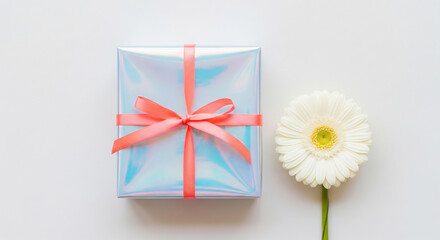 Top view flat lay of an elegant gift box in iridescent wrapping paper with a red ribbon and a white gerbera flower on a white background