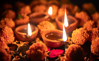 Closeup of Handmade Diwali Clay Diya with Glowing Flames with Marigold Flower Isolated on Black Background, Happy Deepavali or Diwali Festival Concept, Festival of Lights