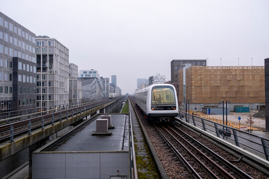 Modern train arriving at elevated platform between contemporary residential blocks under clear blue sky showing integrated mobility design and sustainable public transport system in Orestad Copenhagen