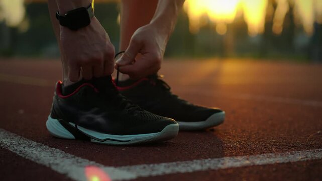 Healthy lifestyle. Active man in sports gear ties shoelaces on a special field. Steady camera movement disciplined athlete puts on running shoes leads an active lifestyle, movement