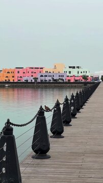 wooden pier with metal railings leading to colorful buildings of mina district in doha qatar