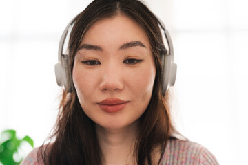 A young woman with headphones on listens intently, her gaze directed downwards as she concentrates on her audio experience.