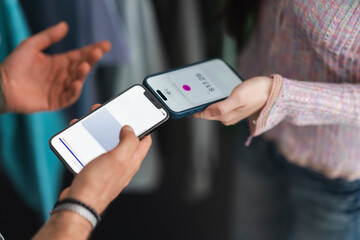 Two people are using their mobile phones to make a contactless payment, one holding a phone with a payment amount displayed.
