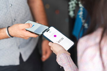 Two people are using their mobile phones to make a contactless payment of seventeen dollars and twenty-five cents.