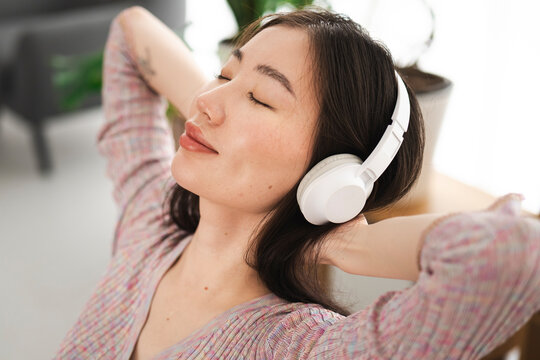 A young woman with her eyes closed enjoys music through her headphones, resting her head back in a moment of relaxation.