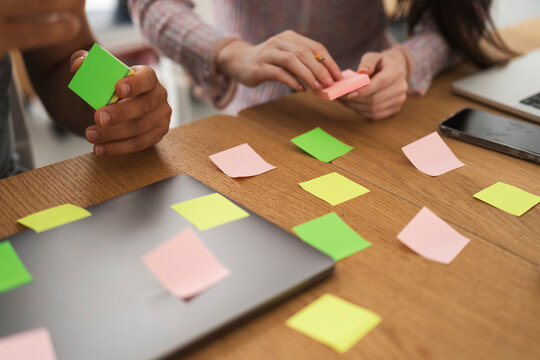 Two people collaborate on a project, using colorful sticky notes and a laptop to brainstorm ideas on a wooden desk.