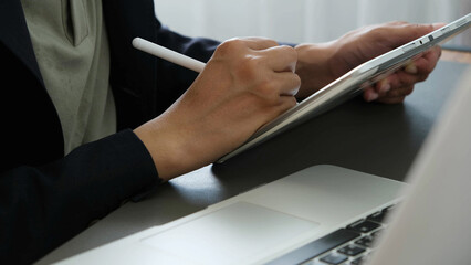 Business professional using digital tablet with stylus for creative work beside laptop on desk