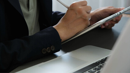 Business professional writing on digital tablet beside laptop in modern office workspace