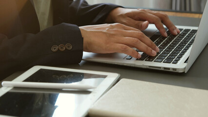 Businessman typing on laptop with digital tablet and notebook on desk, working in modern office environment with focus and concentration
