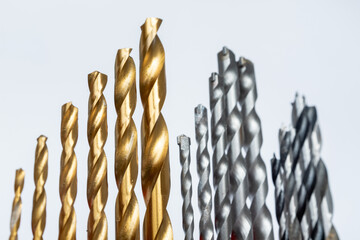 A low-angle, close-up composition of various metal drill bits (HSS and masonry) against a white background, symbolizing power tool accessories, construction work, and professional hardware for technic