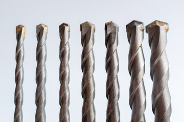 Alignment of seven tungsten carbide-tipped masonry drill bits against a white background: Represents construction tools, hardware, engineering, and DIY repair projects