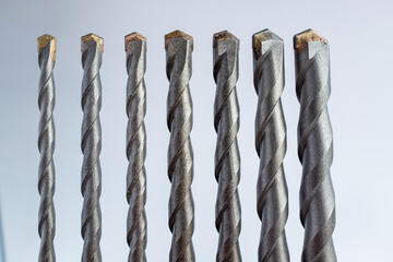 Metal drill bits arranged in a row on a light background, showing industrial tool texture and precision equipment for construction, repair, manufacturing, and hardware design projects