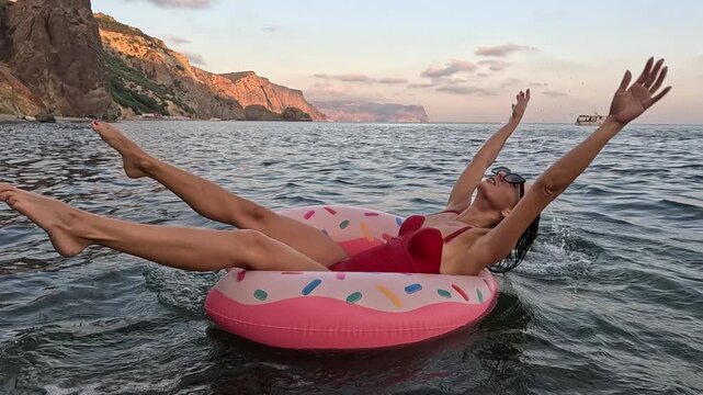 Woman Floating Ocean, young girl relaxes on pink donut in the sea at beautiful sunset.