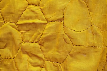Obraz premium Close up view of golden quilted fabric showcasing a textured hexagonal pattern, ideal for backgrounds or design elements