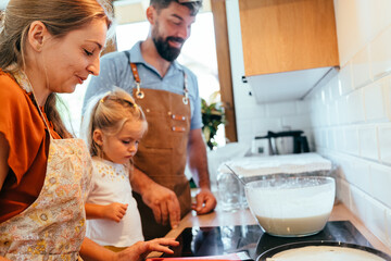 Parents and toddler cooking pancakes together in kitchen