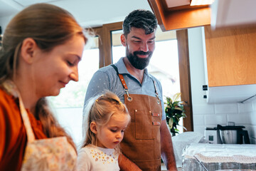 Parents helping toddler cook pancakes at stove in kitchen