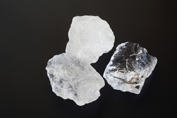 Three pieces of natural alum crystals on black background. Transparent mineral stones used for...