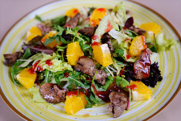 Warm salad with chicken liver in cream sauce with fried potatoes, mushrooms and mixed green salad in a white porcelain plate on a brown wooden table in an elite restaurant. Close-up. High quality