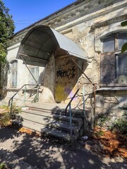 Weathered building entrance with metal canopy and old steps, urban vintage architecture composition, aged stone facade texture, sunlight and shadows, heritage exterior construction detail background.