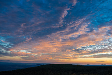 A vibrant sky of blue and orange glows above the dark silhouette of forested hills during a tranquil sunrise or sunset.