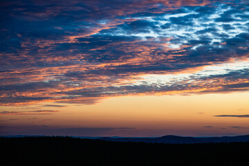 A dramatic sky bursts with layered clouds in vivid hues of blue, purple, orange, and gold during a...