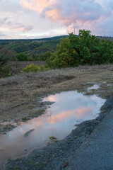 mountain road with puddles reflecting pink clouds