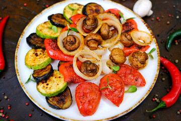 Grilled vegetables: red and yellow paprika, zucchini, eggplant, mushrooms, tomatoes and onions served on rustic wooden cutting board, white table background, top view. High quality photo