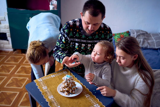 a family with daughters toddler and teenager make a Christmas tree from gingerbread cookies and decorate it with white cream and blue sugar snowflakes