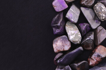 Sugilite heap jewel stones texture on half black background. Pile mineral pebbles background. Place for text.