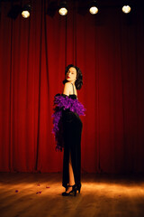 Dancer in a black gown with purple feathers performs on stage under spotlight in a theater setting