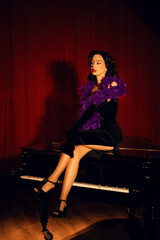 Performing artist in a purple feather boa poses on a grand piano with red curtains in the background during a glamorous evening event