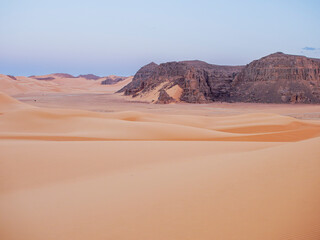 Landscape of the Red Tadrart with dunes and rock formations at sunrise in the Sahara Desert, Algeria.
