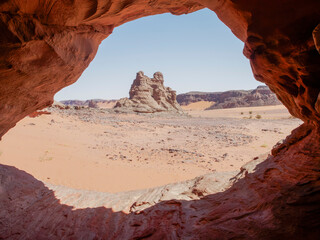 Desert landscape of the Red Tadrart with rock formations and golden sand under a blue sky. Natural scenery of the Algerian Sahara.