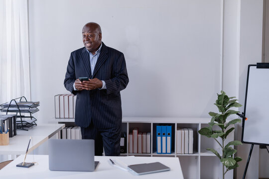Senior African American businessman surprised by new technology, standing and holding a smartphone in a modern corporate office environment, reflecting innovation and professional communication
