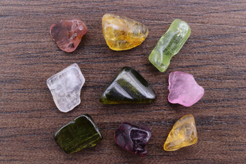 Tourmaline different color jewel stone texture on brown varnished wood background. Macro closeup.